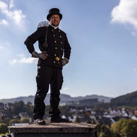Foto eines hockenden Mannes in Schornsteinfeger-Kleidung